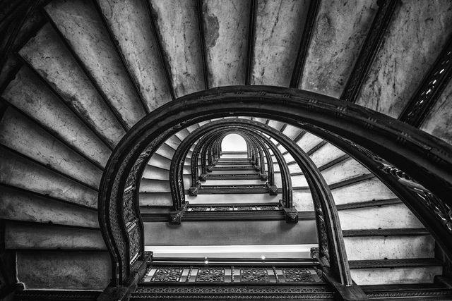 Looking up through the center of an ornate spiral staircase, its arches repeating and ascending