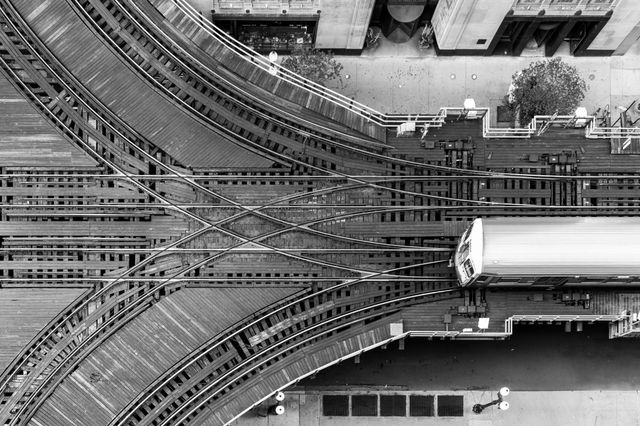 An aerial view straight down onto a web of elevated train tracks and switches, with a train approaching