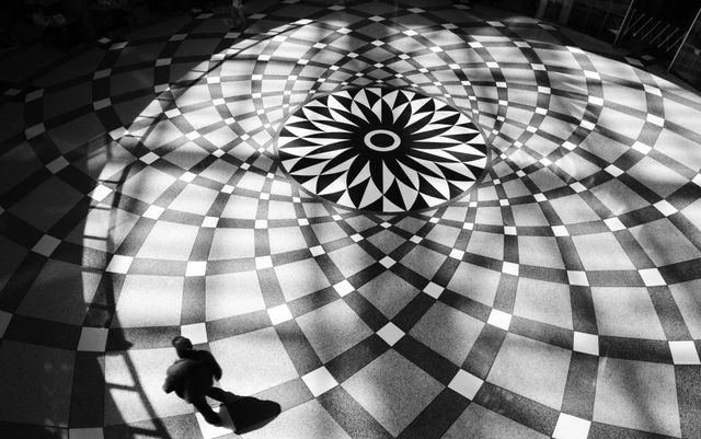 An overhead view of a radial checkerboard floor pattern with a single person walking through it